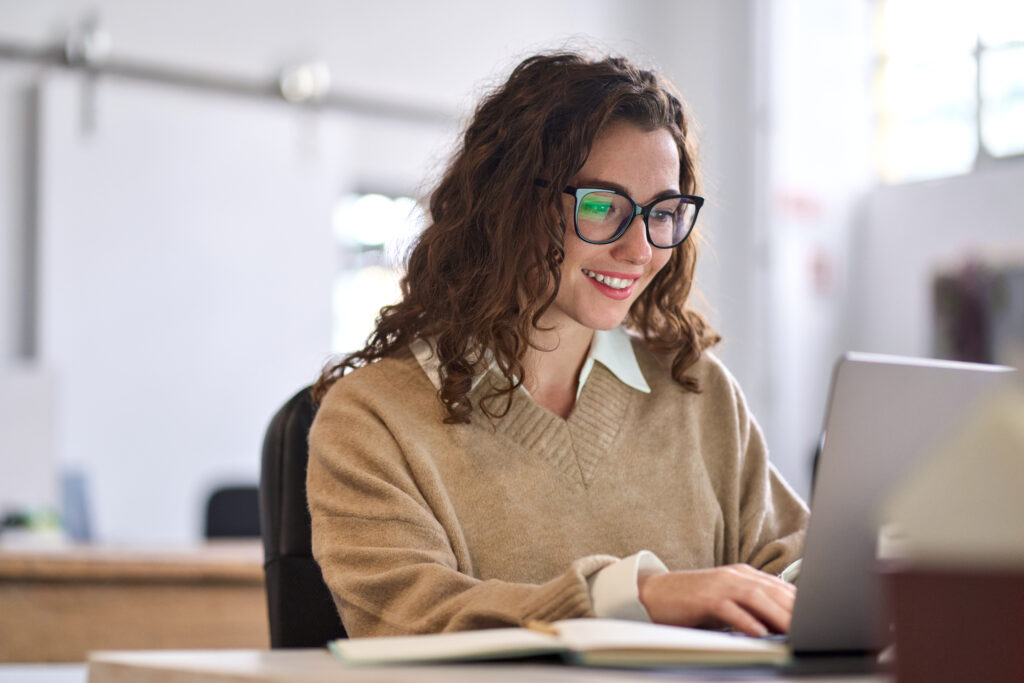 Frau mit Brille sitzt vor Notebook und lächelt