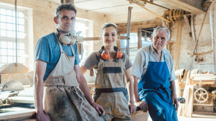 Drei Schreinereimitarbeitende in Arbeitskleidung posieren in einer Werkstatt.